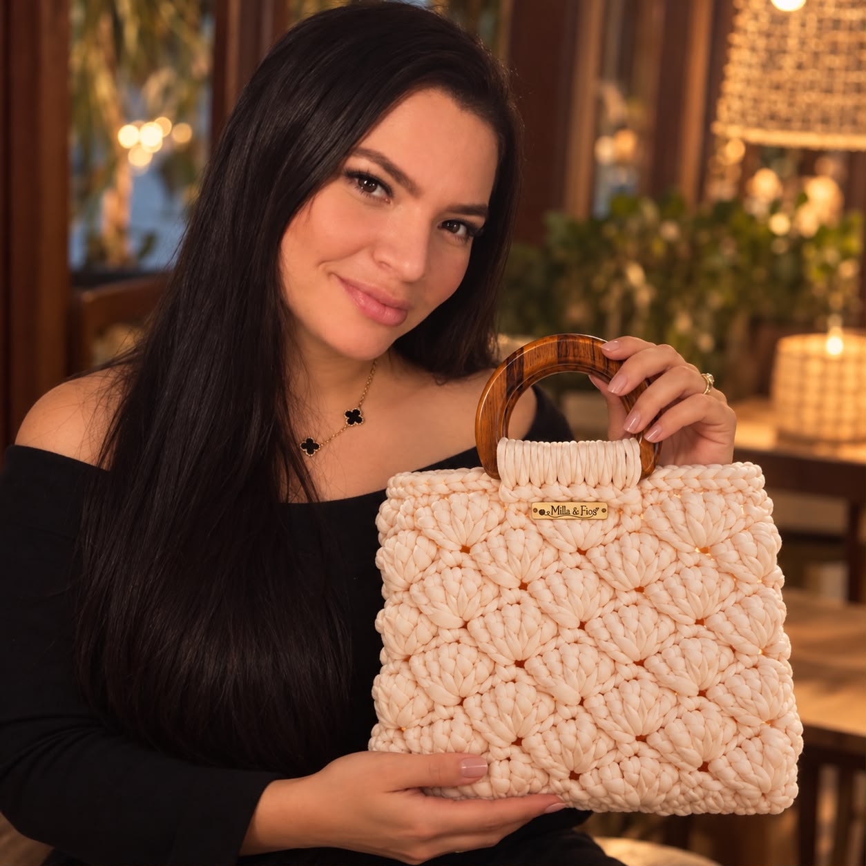 Uma bolsa creme sendo segurada, mostrando o relevo dos pontos e a alça de madeira